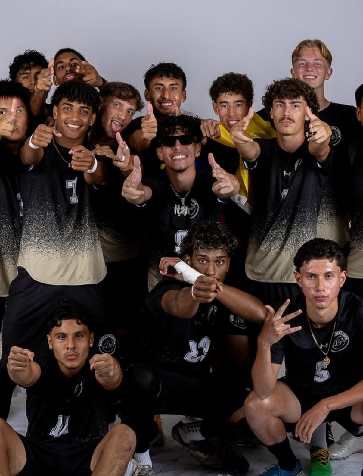 Des joueurs de soccer en maillots noir et doré posent ensemble pour une photo d'équipe, sourires et pouces levés